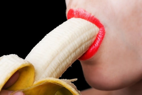 Frau mit roten Lippen führt eine Banane tief in den Mund. Darstellung der Deepthroat-Technik mit einer Banane zur Veranschaulichung der Technik und Tiefe.