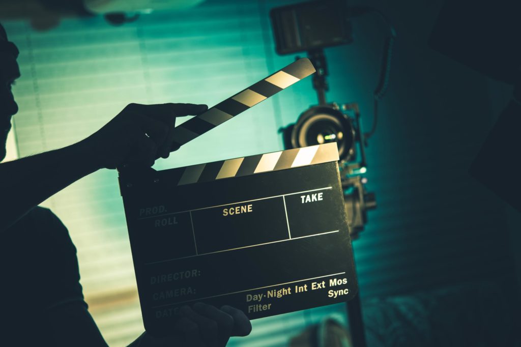Ein Regisseur hält eine Filmklappe vor einer Kamera – hochwertige Produktion und professionelle Standards in der Erotikbranche.